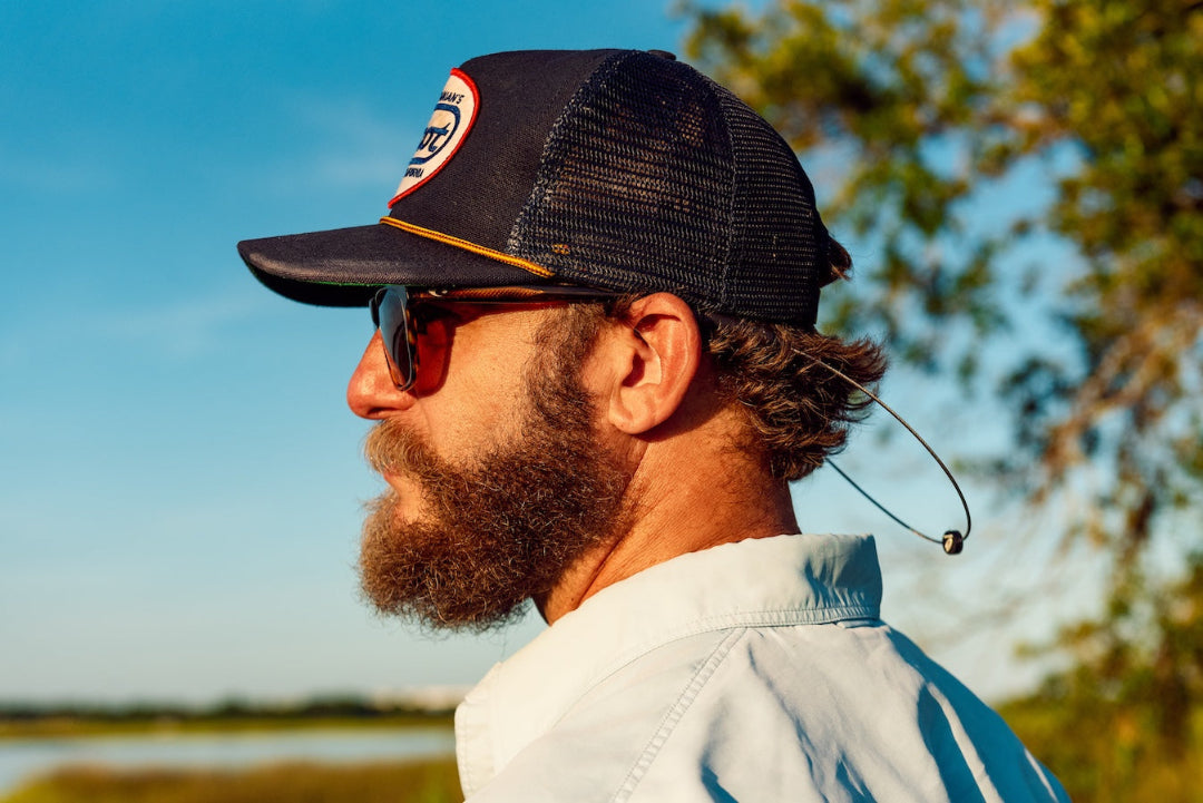 Side view of a bearded man in a trucker hat and sunglasses with GRAPLRZ grey sunglass retainers attached