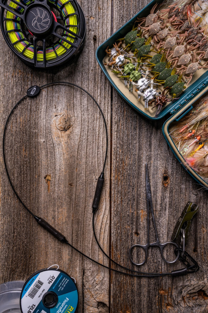 Black GRAPLRZ VERZA Multi Use Lanyard surrounded by various fishing items on a wood background