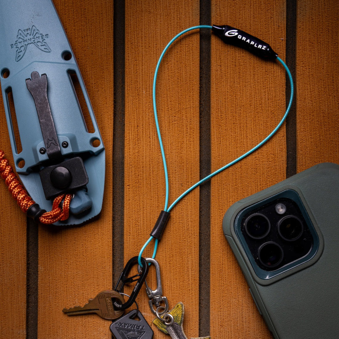 Aqua GRAPLRZ Verza Mini Utility Lanyard clipped to keys on a wood background surrounded by various items