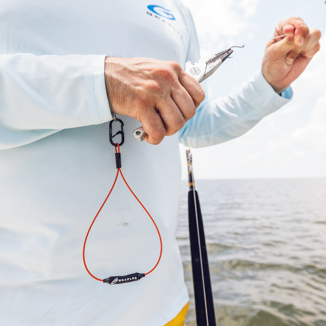 Person in long sleeved shirt using pliers with orange GRAPLRZ Verza Mini Utility Lanyard attached