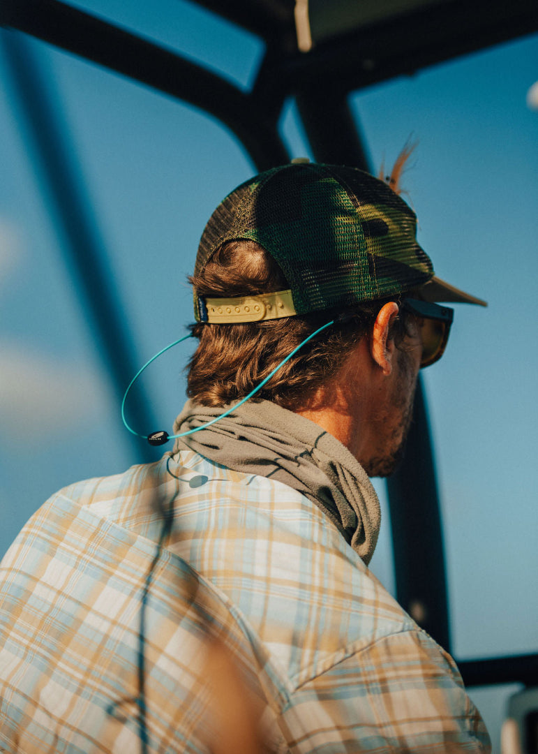 Man with his back turned in a camouflage trucker hat and aqua GRAPLRZ sunglass retainers