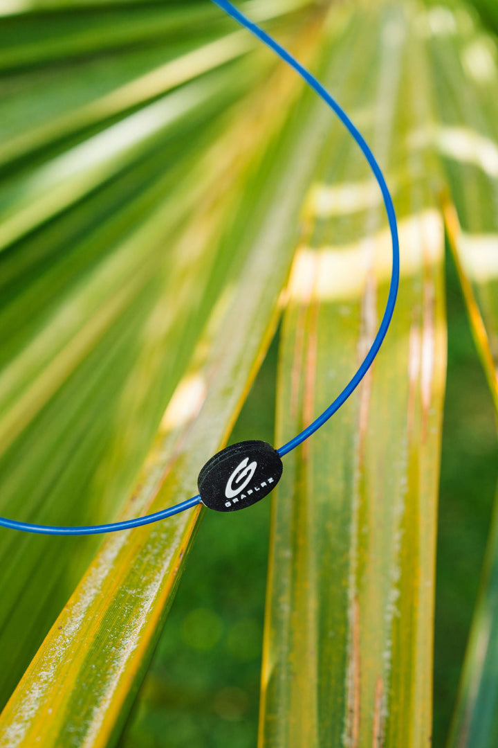 Blue GRAPLRZ Original Sunglass Retainers in front of tropical leaves