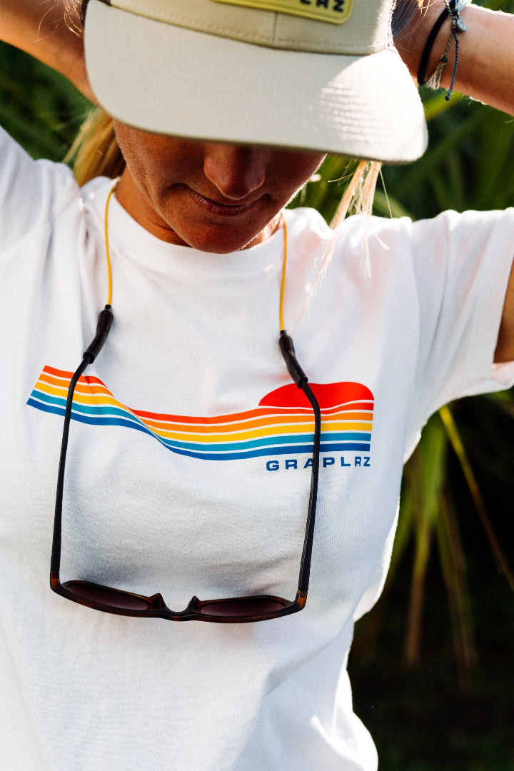 Woman wearing white Women's Sunset Tee and yellow GRAPLRZ sunglass strap looking down
