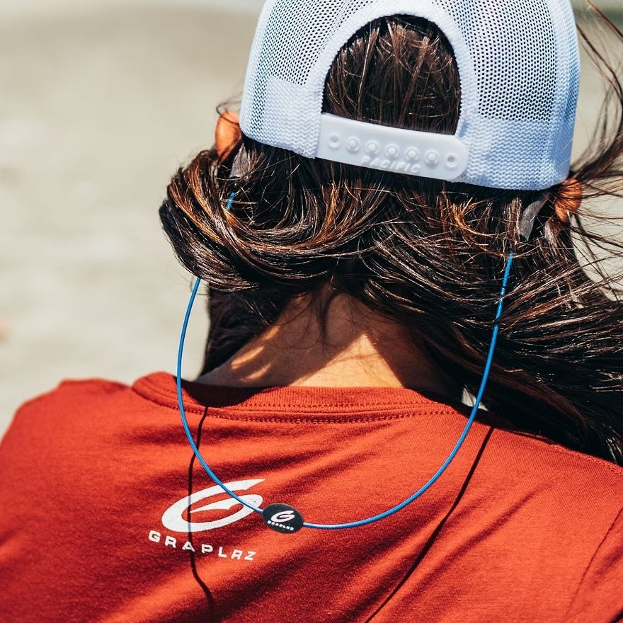 Close up of blue GRAPLRZ sunglass retainers on a woman with her back turned against a strong wind