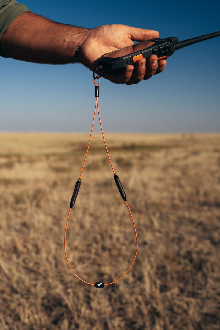 Hand holding walkie talkie clipped to orange GRAPLRZ VERZA Multi Use Lanyard