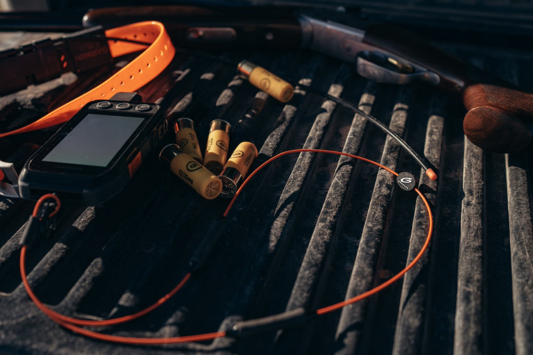 Orange Verza Mini Utility Lanyard clipped to a camera in a truck bed filled with shotgun bullets