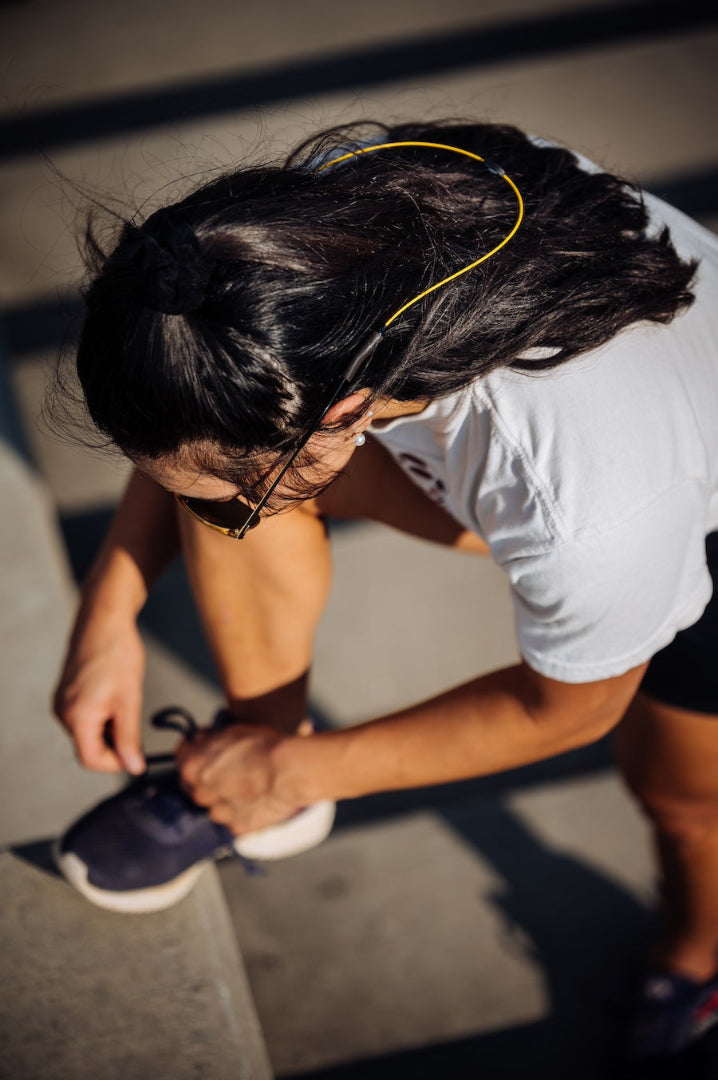 Woman tying her shoes on a staircase wearing yellow GRAPLRZ sunglass retainers