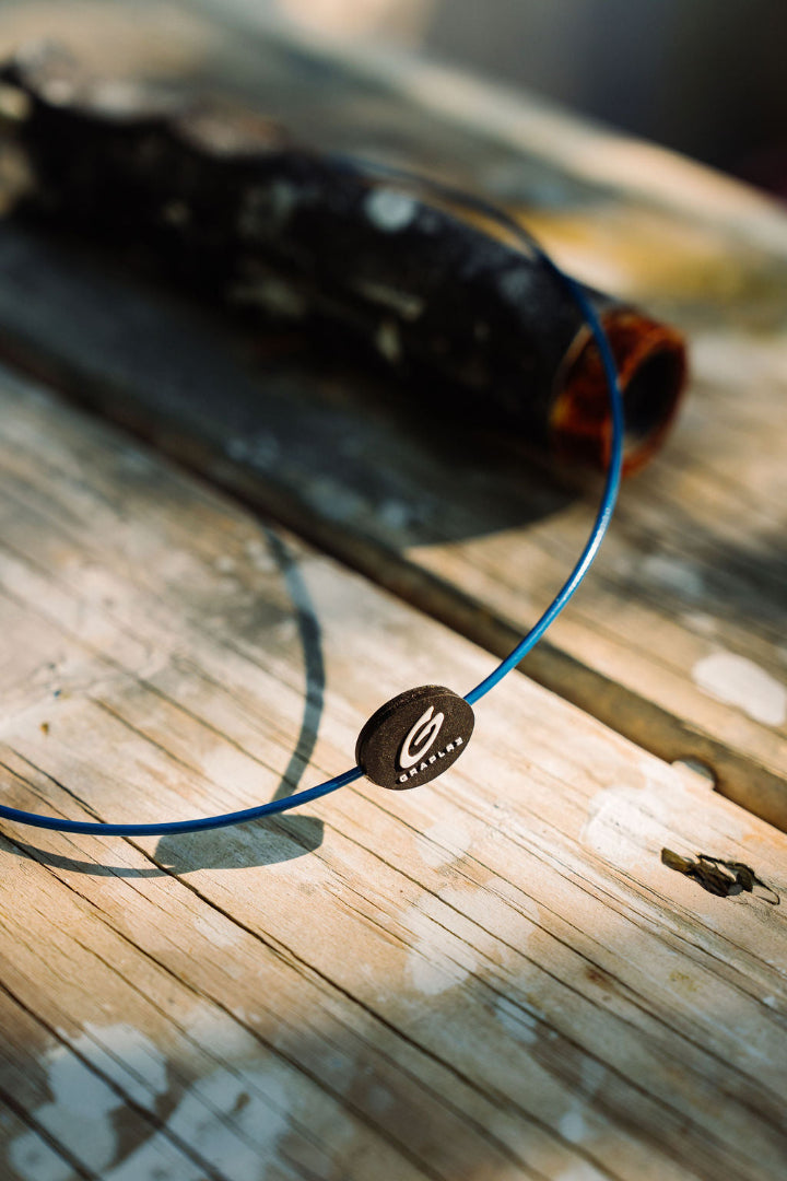 Blue GRAPLRZ sunglass retainer on a wooden dock with fishing rod in background